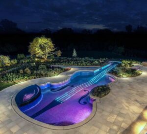 A unique custom violin-shaped pool with vibrant LED lighting at night, designed and built by Purpose Pools in Henderson, NV.