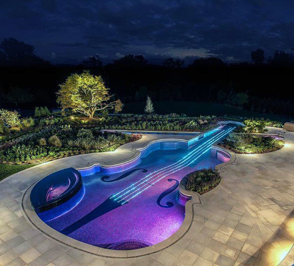 A unique custom violin-shaped pool with vibrant LED lighting at night, designed and built by Purpose Pools in Henderson, NV.