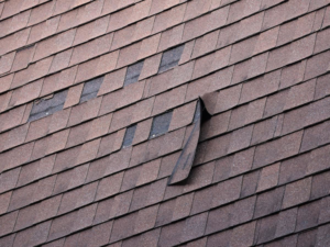 A damaged asphalt shingle roof with missing and lifted shingles, indicating potential water damage issues, by Emanuel Roofing LLC in Huron, SD.