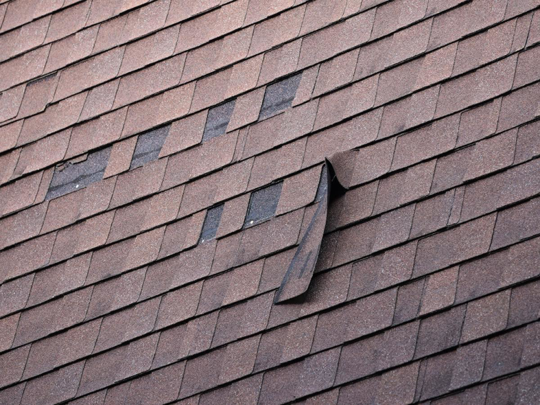 A damaged asphalt shingle roof with missing and lifted shingles, indicating potential water damage issues, by Emanuel Roofing LLC in Huron, SD.