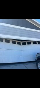 A severely damaged and bent white garage door requiring repair from A-1 Garage Door Repair in Syracuse, UT.