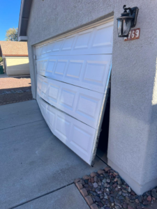 A severely damaged and bent white garage door on a residential home, requiring repair or replacement by A1 Garage Guy Wes in Picture Rocks, AZ.