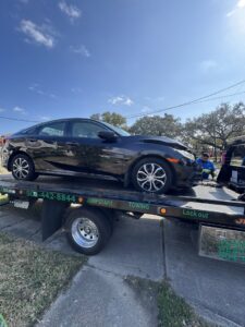 A damaged black car being transported on a flatbed tow truck by ABOD Towing LLC in New Orleans, LA.