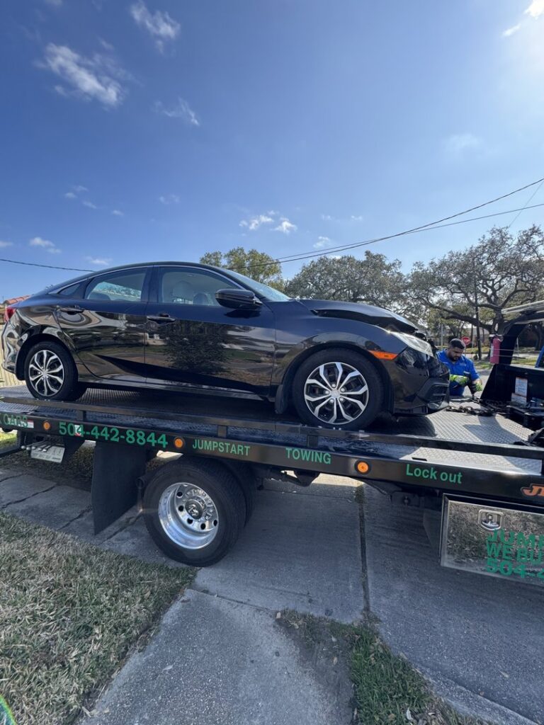 A damaged black car being transported on a flatbed tow truck by ABOD Towing LLC in New Orleans, LA.