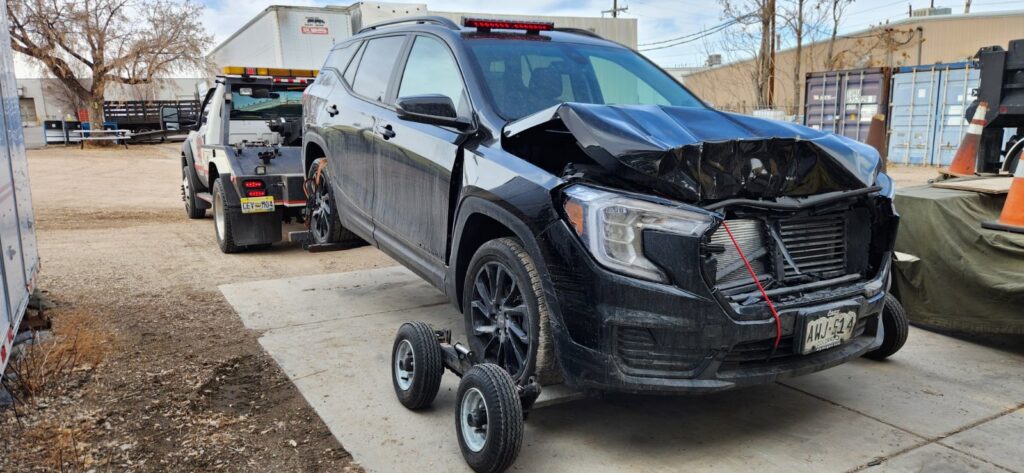 A damaged black SUV being towed by a wheel-lift tow truck with dollies from A-ROD Towing in Denver, CO.