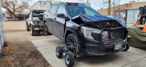 A damaged black SUV being towed by a wheel-lift tow truck with dollies from A-ROD Towing in Denver, CO.