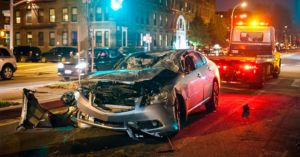 A severely damaged car after an accident, with a tow truck ready to assist from Atlantis Towing Services in Chicago, IL.