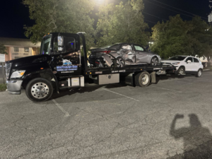 A tow truck from Southeastern Towing and Transport towing a damaged car and an SUV at night in Savannah, GA.