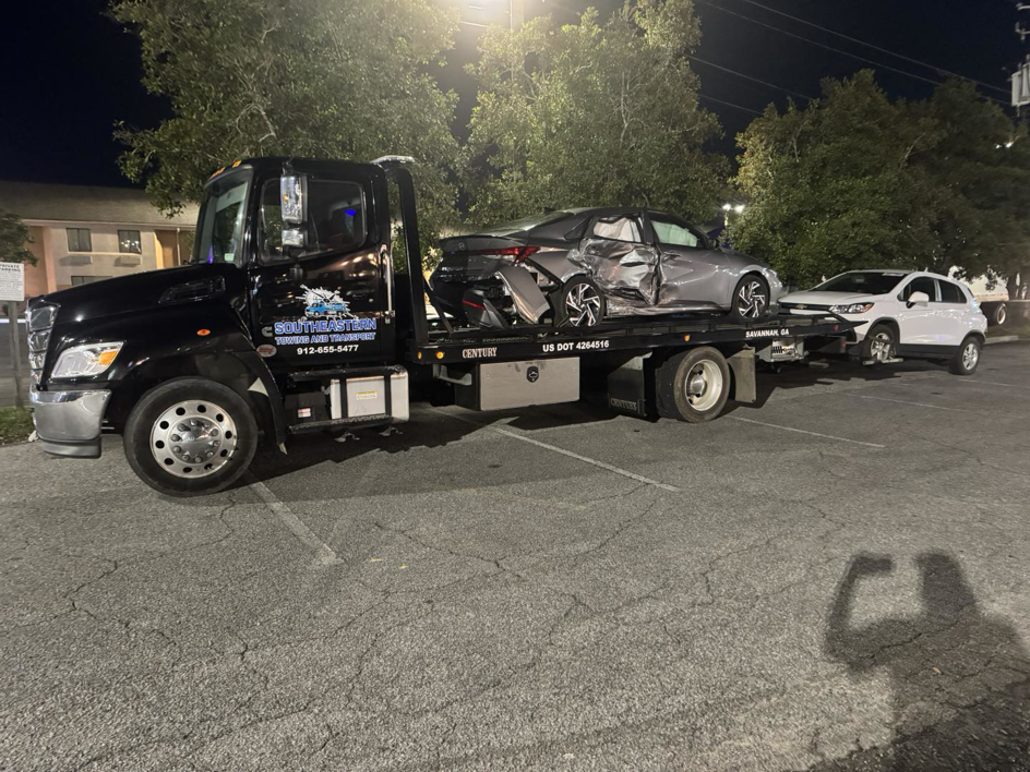 A tow truck from Southeastern Towing and Transport towing a damaged car and an SUV at night in Savannah, GA.