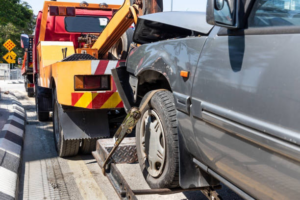 A damaged grey car being towed by a wheel-lift tow truck from Buckeye Riverside Towing in Cincinnati, OH.