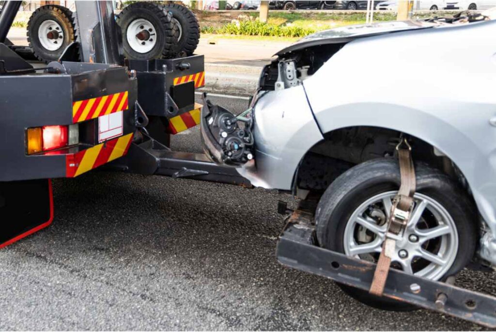 A heavily damaged silver car being towed by a wrecker tow truck for Spokane Towing Services in Spokane, WA.