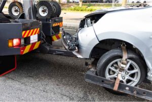 A heavily damaged silver car being towed by a wrecker tow truck for Spokane Towing Services in Spokane, WA.