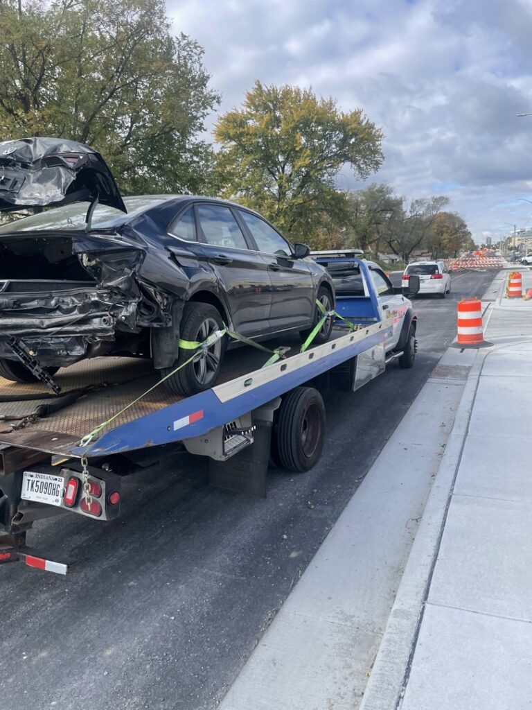 A damaged black car loaded onto a flatbed tow truck by Mr.Quickpick Roadside Assistance in Indianapolis, IN.