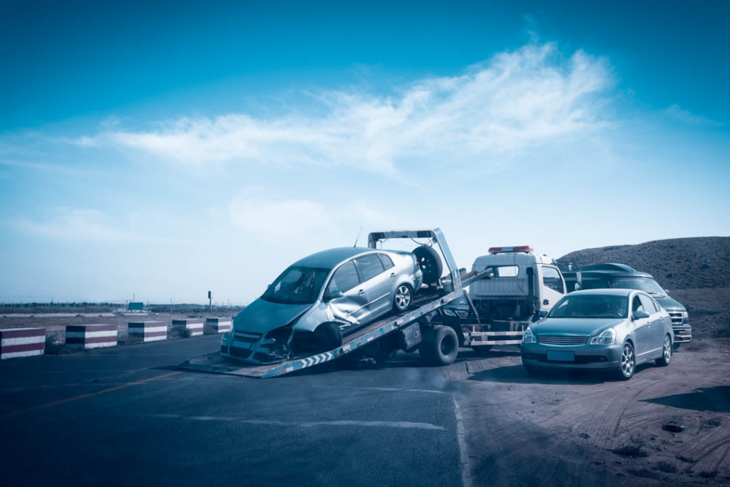 A damaged silver car being towed on a flatbed tow truck after an accident by On Time Towing Houston, TX.