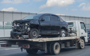 A heavily damaged black car being transported on a flatbed tow truck by Windy's Collision Center, Inc. in Saint Paul, MN.