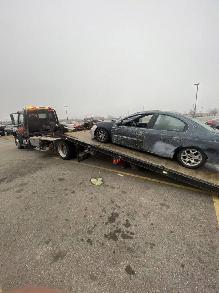 A damaged dark car being loaded onto a flatbed tow truck by Jensen Towing in Kenosha, WI.