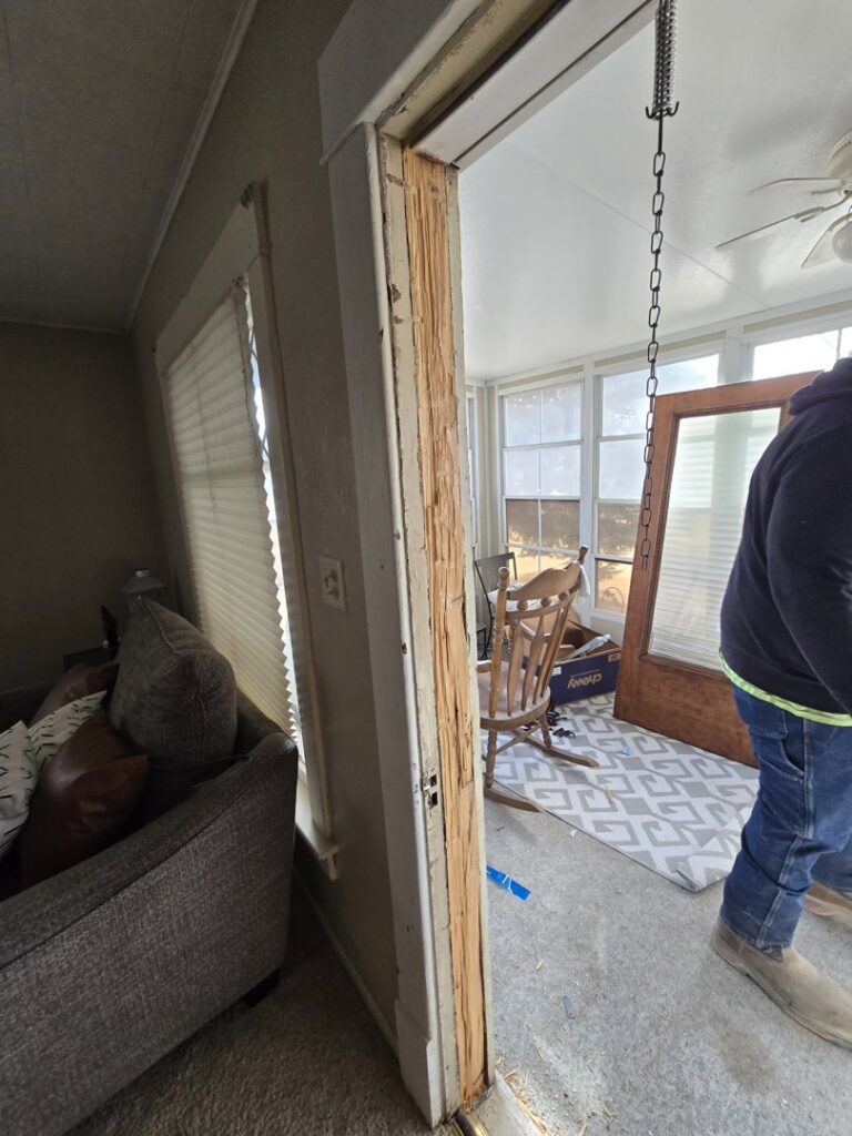 A severely damaged wooden door frame, likely from water damage, awaiting repair by Grand Rising Group in Mitchell, SD.