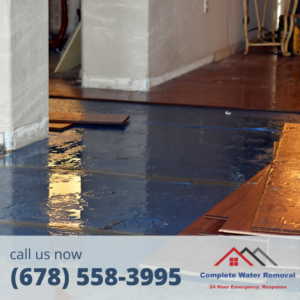 A damaged floor with standing water and loose wood planks, showing a water damage restoration job by Complete Water Removal and Restoration in Cumming, GA.