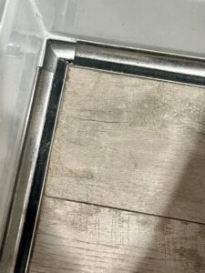 A close-up of a damaged floor trim corner with visible water stains and discoloration, indicating a water damage problem for Ciocca Cleaning & Restoration in Fort Wayne, IN.