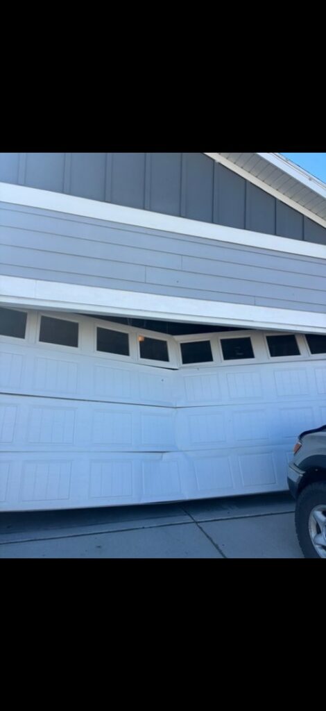 A severely damaged garage door, bent and off its tracks, requiring repair by A-1 Garage Door Repair in Syracuse, UT.