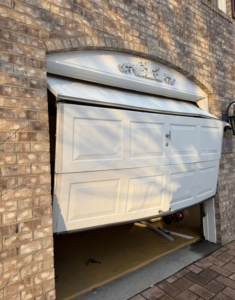 A severely damaged white garage door requiring repair or replacement by Mascolo Overhead Doors & Maintenance in Brookfield, CT.