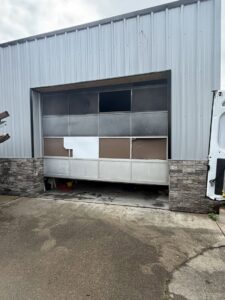 A damaged garage door on a metal building, indicating a repair or replacement service by 4thgenerationsdoors in Huntington, WV.