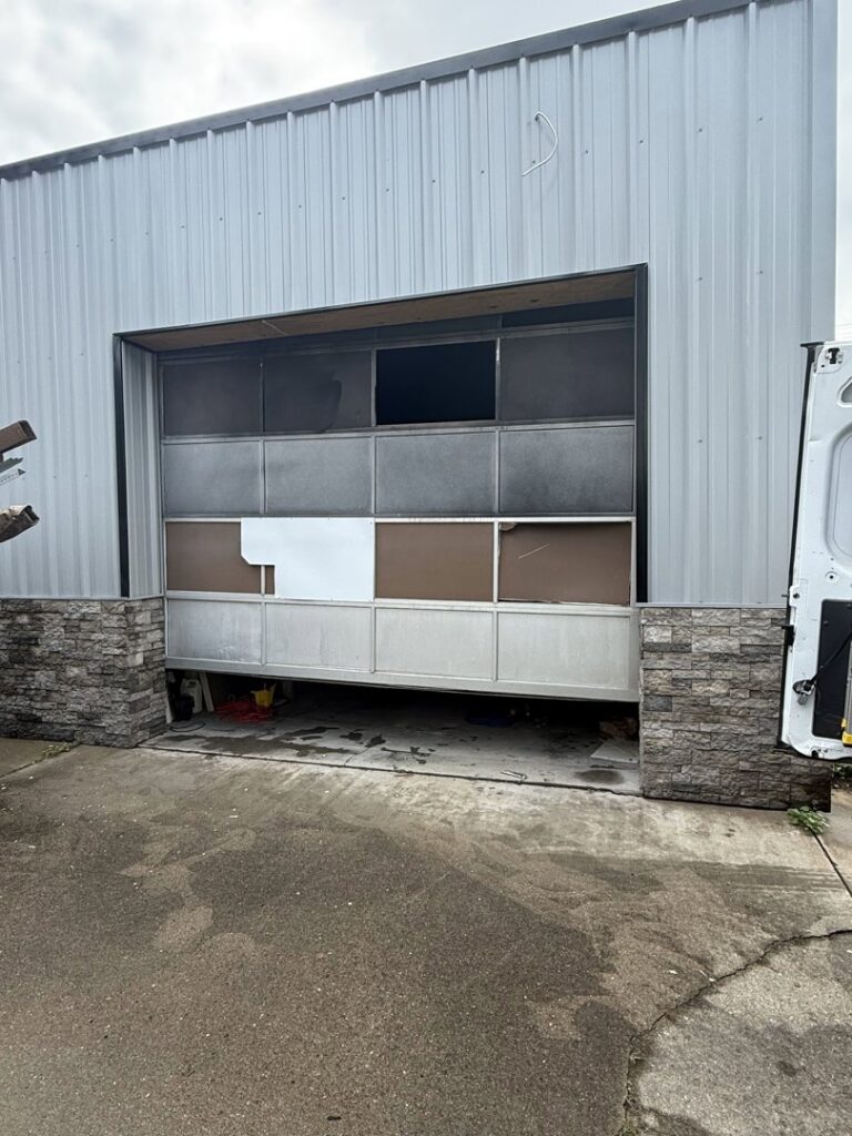 A damaged garage door on a metal building, indicating a repair or replacement service by 4thgenerationsdoors in Huntington, WV.