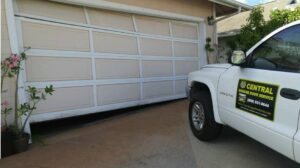 A Central Garage Door Service truck at a residence in Kapolei, HI, with a damaged garage door requiring repair.