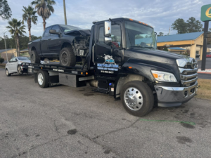 A black tow truck from Southeastern Towing and Transport towing a damaged pickup truck and another car in Savannah, GA.