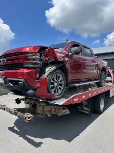 A damaged red pickup truck being transported on a flatbed tow truck by RonniesTowing&Recovery in Bryan, TX