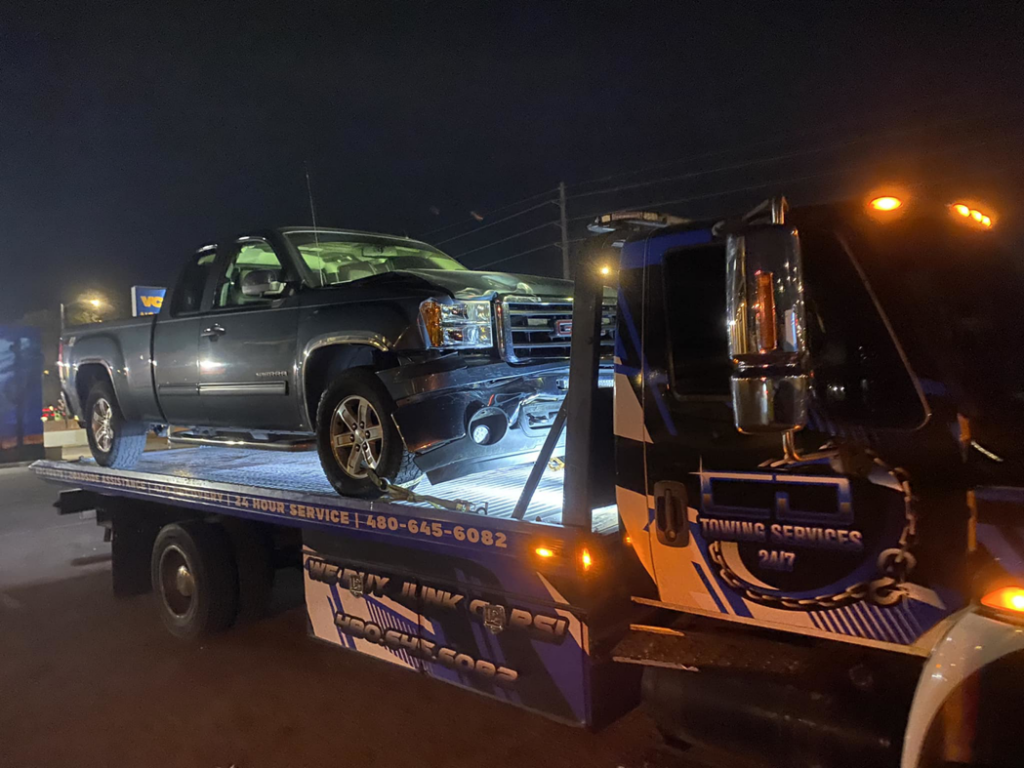 A damaged dark grey pickup truck being towed on a flatbed truck by CnD towing in Phoenix, AZ.