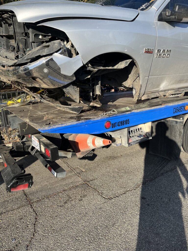 A damaged silver Ram 1500 pickup truck being towed on a blue flatbed tow truck by A&A Towing Services in Bakersfield, CA.