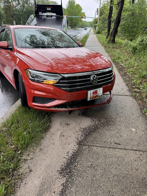 A damaged red car with its front bumper detached, parked on a sidewalk with a tow truck visible in the background, handled by Ricky's Towing & Recovery LLC in Derwood, MD.