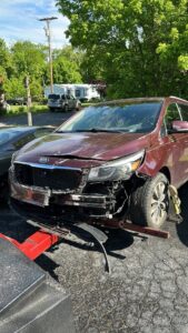 A damaged red Kia minivan being prepared for towing by Tow Truck Company in Johnson City, TN.