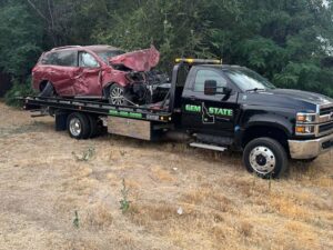 A severely damaged red SUV being recovered on a flatbed tow truck by Gem State Towing and Recovery in Caldwell, ID.