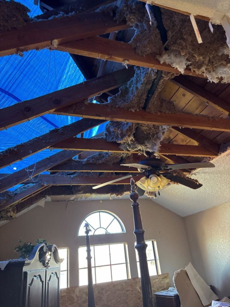 A damaged roof and ceiling with exposed insulation and a blue tarp, indicating water intrusion, handled by Service Professionals in Edmond, OK.
