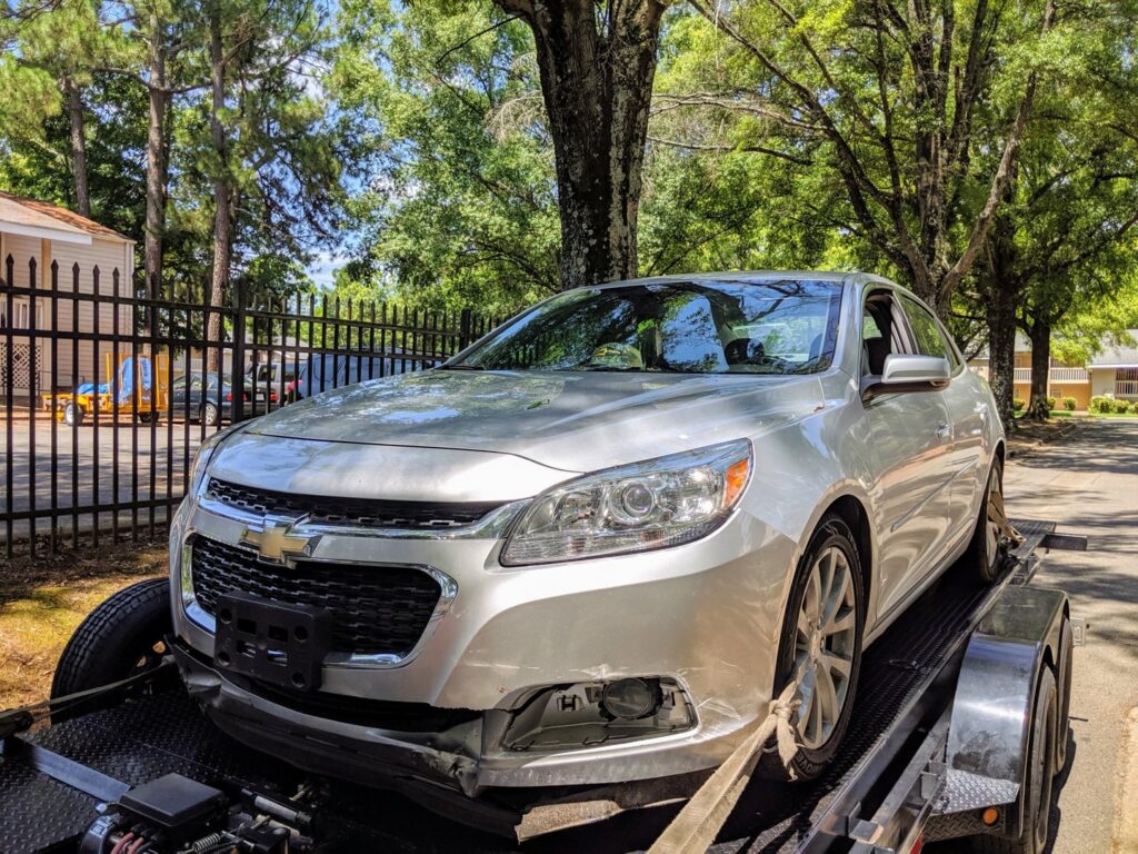 A damaged silver sedan being transported on a car trailer by Snoork Towing in Charlotte, NC.