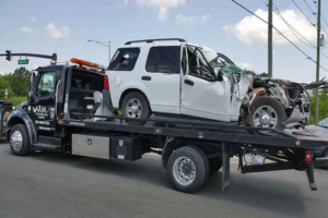 A heavily damaged white SUV being transported on a flatbed tow truck by Cash for junk cars Fort Lauderdale in Fort Lauderdale, FL.