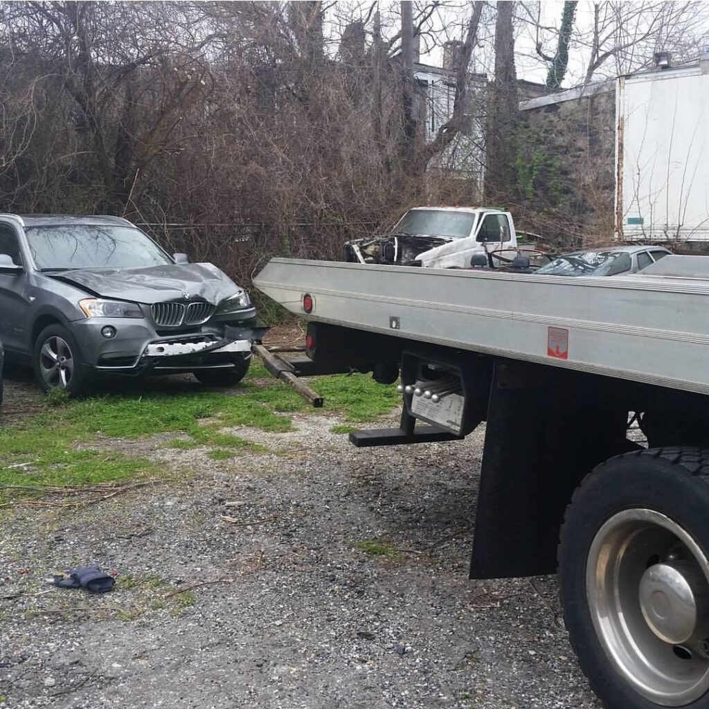 A damaged gray SUV with a Whitelock Towing flatbed truck on site in Baltimore, MD, for accident recovery.