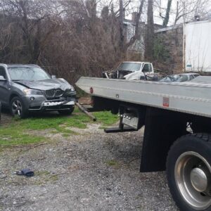A damaged gray SUV with a Whitelock Towing flatbed truck on site in Baltimore, MD, for accident recovery.