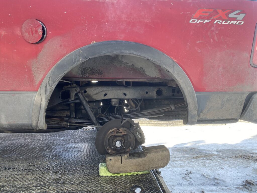 A damaged truck wheel and brake assembly being transported on a flatbed tow truck by Black Mamba Towing & Recovery Llc in Aurora, CO.