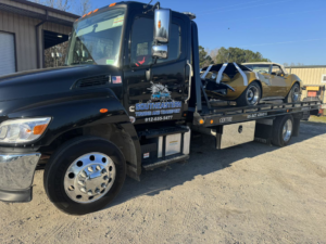 A damaged vintage gold car being transported on a flatbed tow truck by Southeastern Towing and Transport in Savannah, GA.