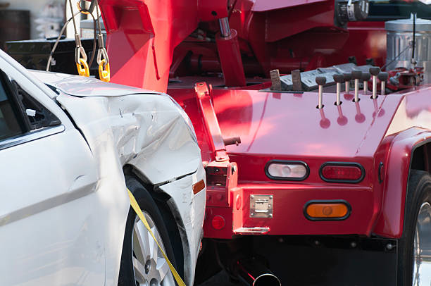 A damaged white car being hooked up to a red tow truck for service by Jensen Towing in Kenosha, WI.
