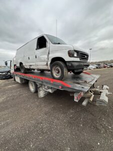 A damaged white cargo van being transported on a flatbed tow truck by Anytime towing services in Columbus, OH.