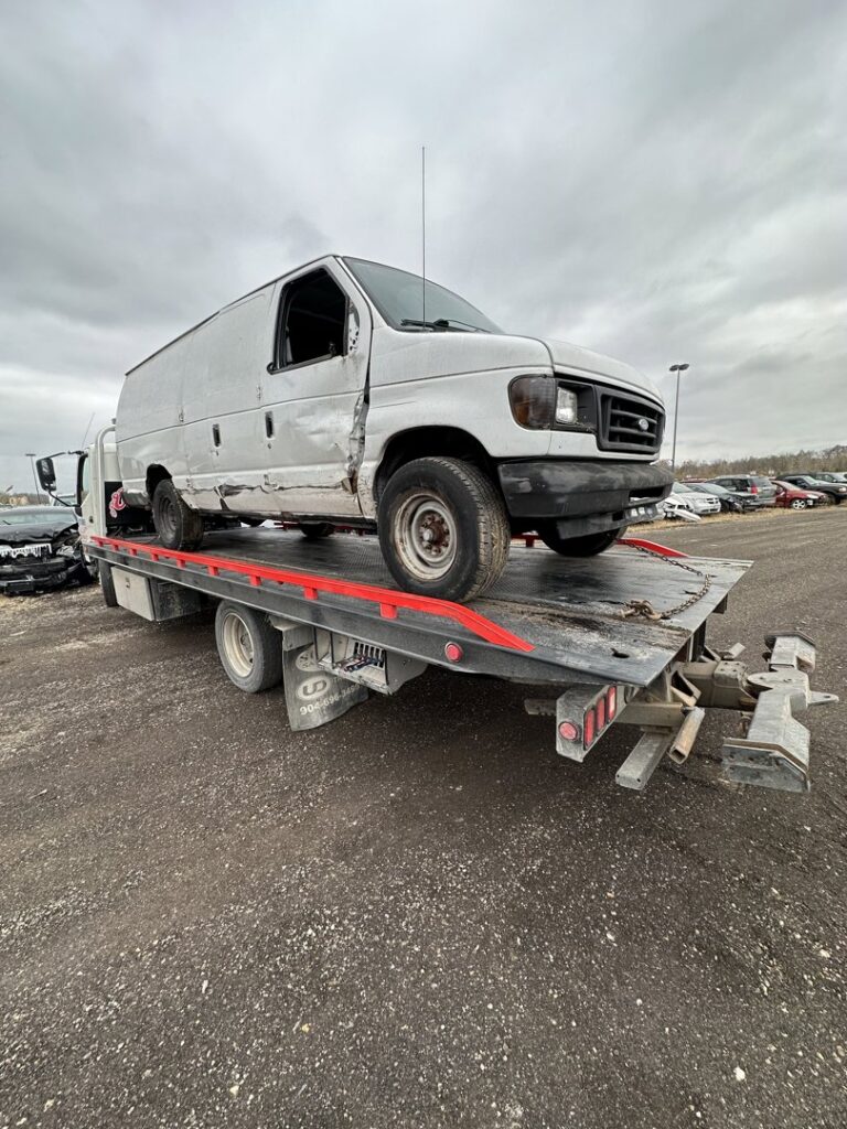 A damaged white cargo van being transported on a flatbed tow truck by Anytime towing services in Columbus, OH.