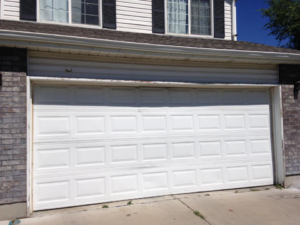 A white garage door with visible damage on the bottom panel, needing repair by Alpine Overhead Garage Door Service in Layton, UT.