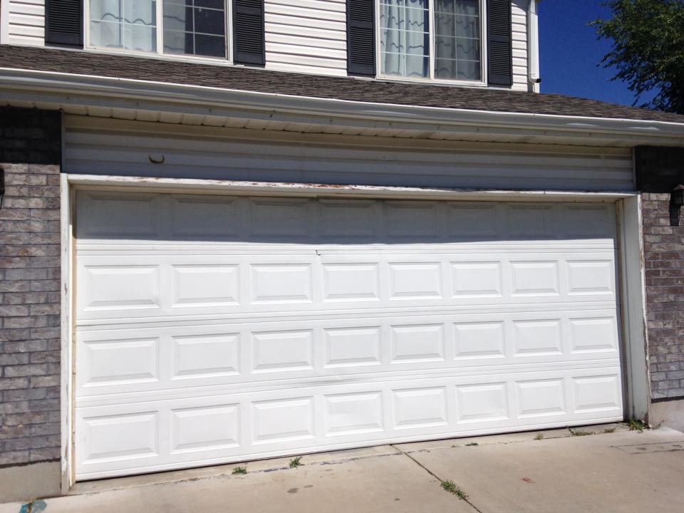 A white garage door with visible damage on the bottom panel, needing repair by Alpine Overhead Garage Door Service in Layton, UT.