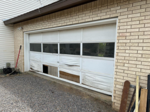 A severely damaged white garage door in need of repair or replacement by Espada Garage Door and Gate, LLC in Las Cruces, NM.