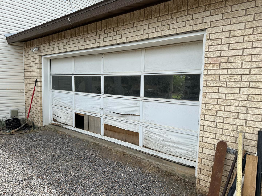 A severely damaged white garage door in need of repair or replacement by Espada Garage Door and Gate, LLC in Las Cruces, NM.