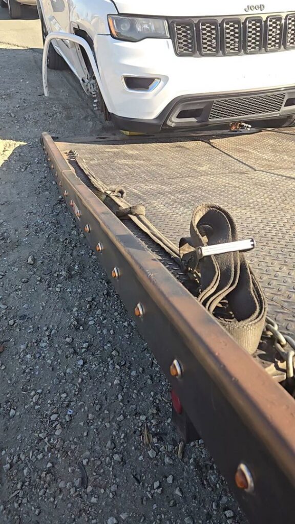 A damaged white Jeep secured with straps on a flatbed tow truck by Ibanez Towing Service LLC in San Jose, CA.